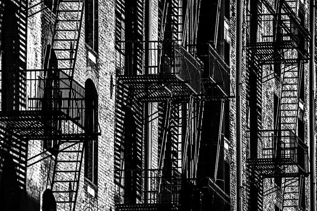 Escaleras de incendios en una fachada de ladrillo, repetidas en profundidad, en blanco y negro.