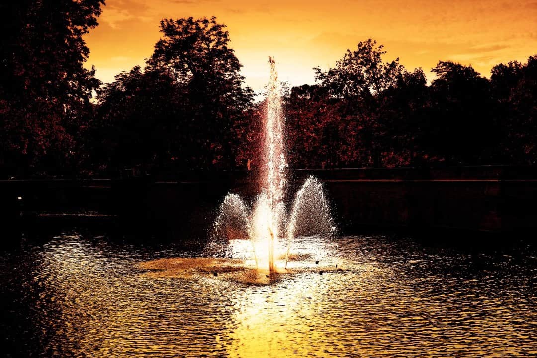 Fuente de un estanque a contraluz al atardecer, con el cielo y el agua virados a naranja.