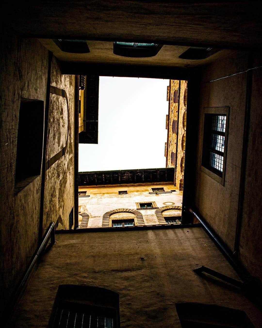 Patio interior de un palacio visto desde un pasadizo en penumbra, con la luz entrando por el vano.