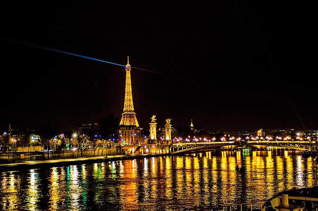 París de noche desde el Sena, con la torre Eiffel iluminada y los reflejos dorados de la orilla sobre el agua.