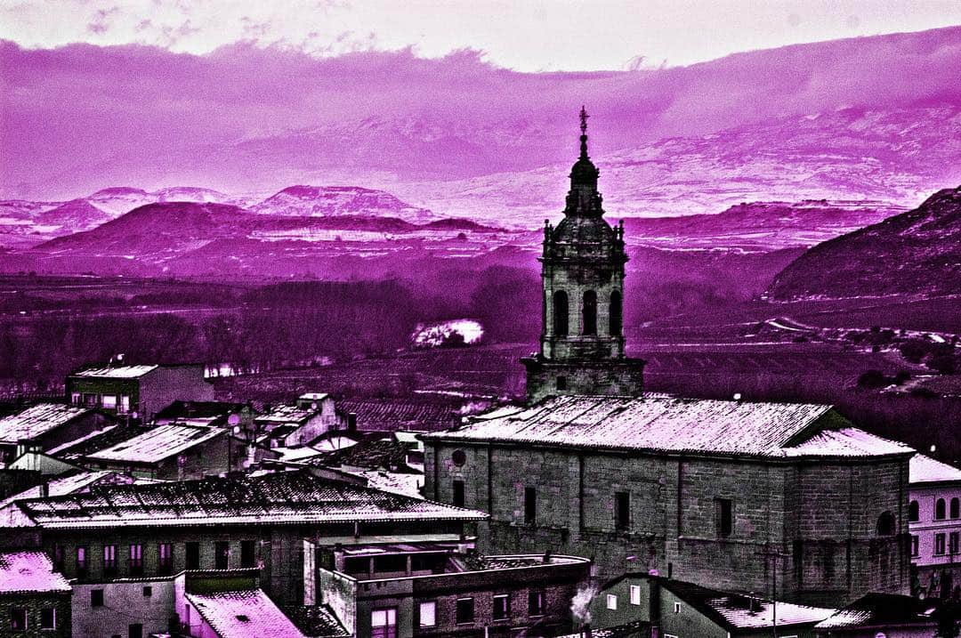 Pueblo con una torre de iglesia y montañas al fondo, con toda la imagen virada a violeta.