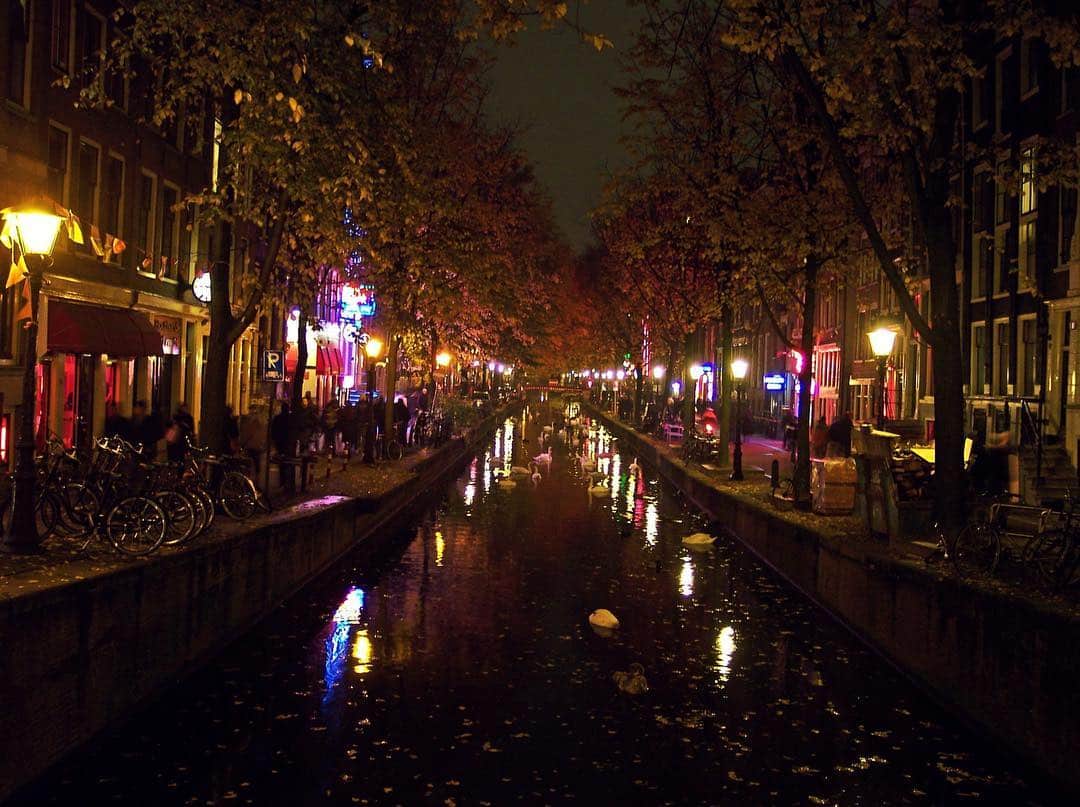 Canal del Barrio Rojo de Ámsterdam de noche, con los reflejos rojos y de neón de la orilla sobre el agua.