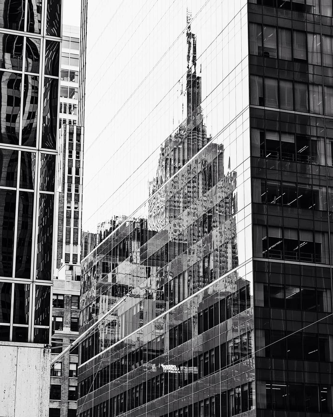 Reflejo del Empire State en la fachada acristalada de otro edificio, en blanco y negro.