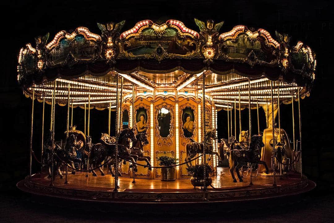 Carrusel antiguo iluminado, con sus caballos y espejos, sobre un fondo oscuro.