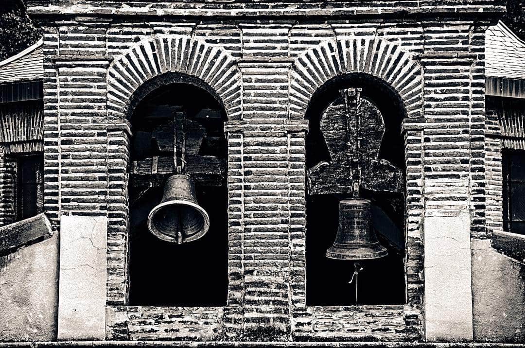 Espadaña de ladrillo con dos campanas bajo arcos de medio punto, en blanco y negro.