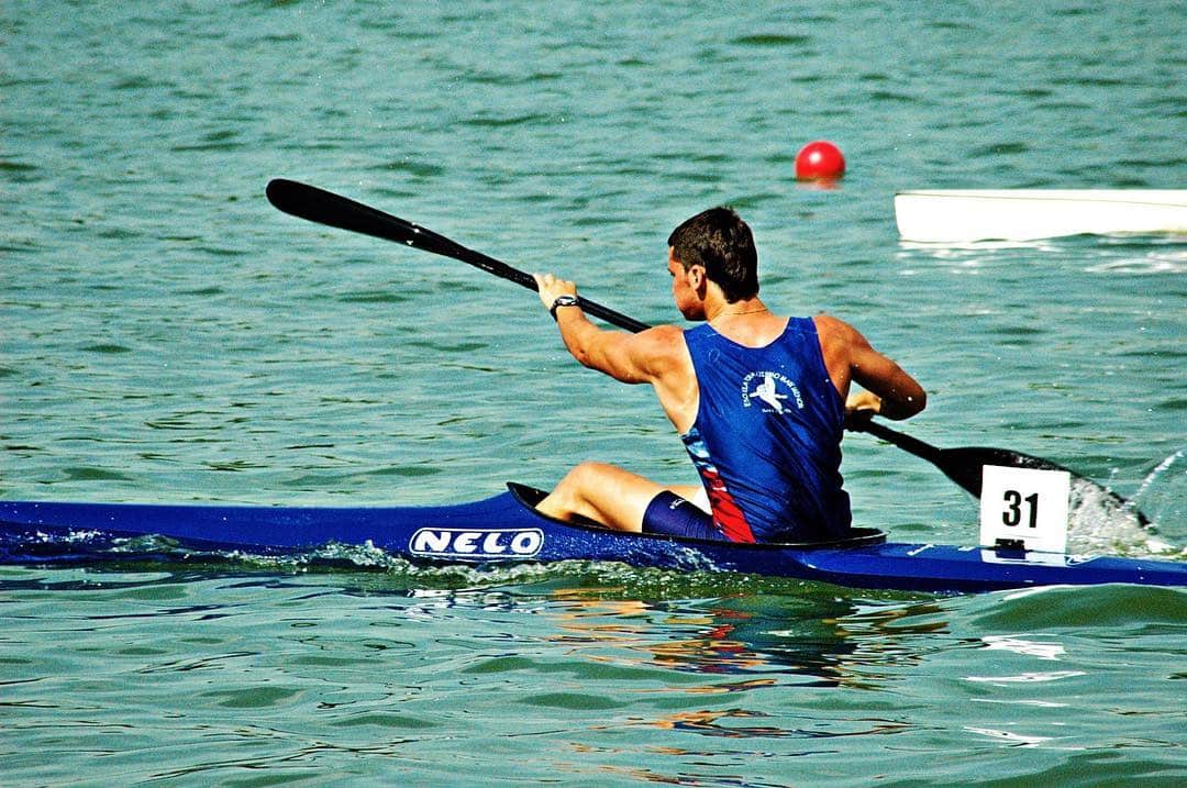 Piragüista con maillot azul y rojo remando en aguas verdes, con el dorsal 31 en la embarcación.