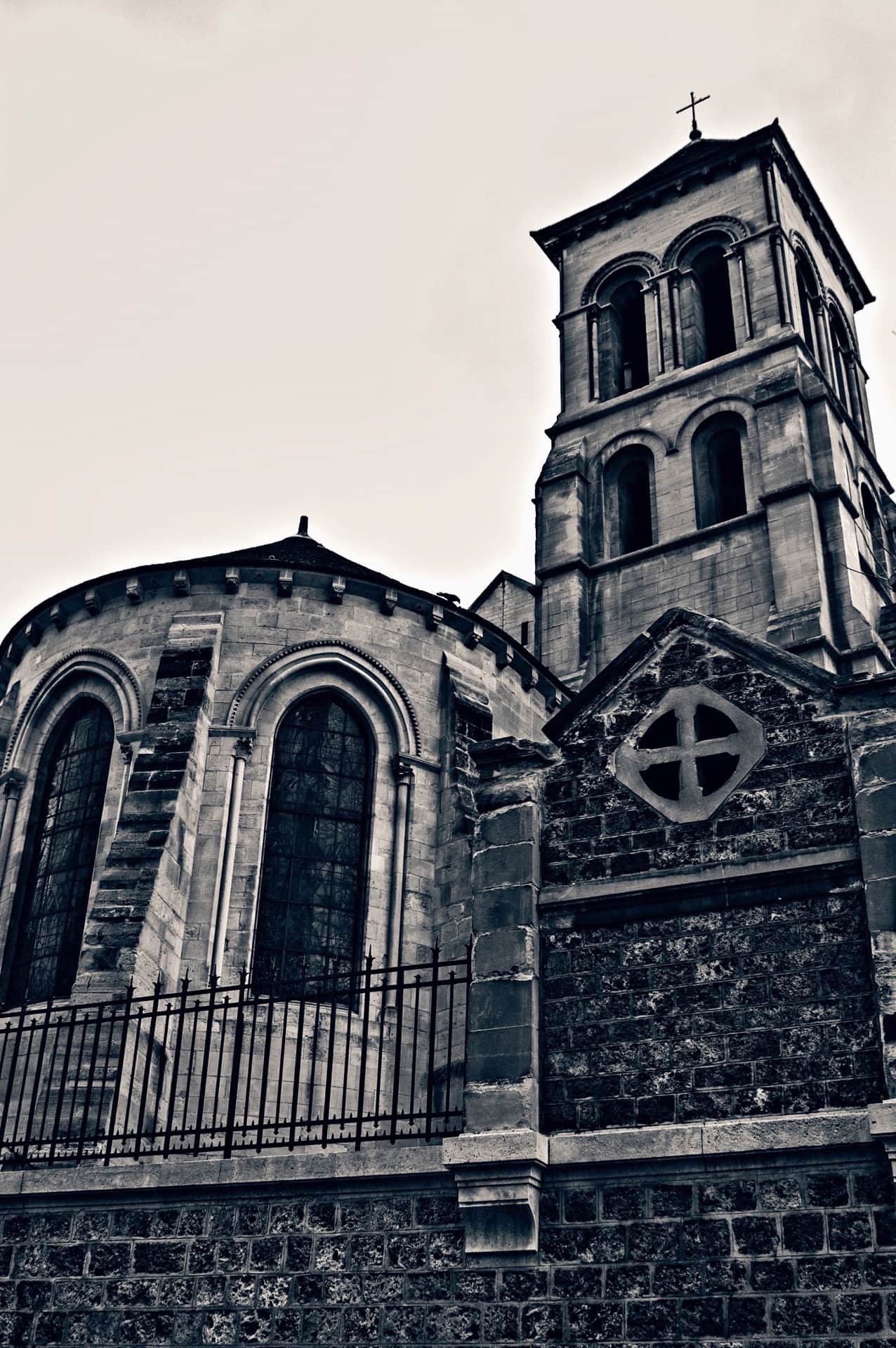 Ábside y campanario de una iglesia de piedra en contrapicado, tras una verja de hierro, en blanco y negro muy contrastado.
