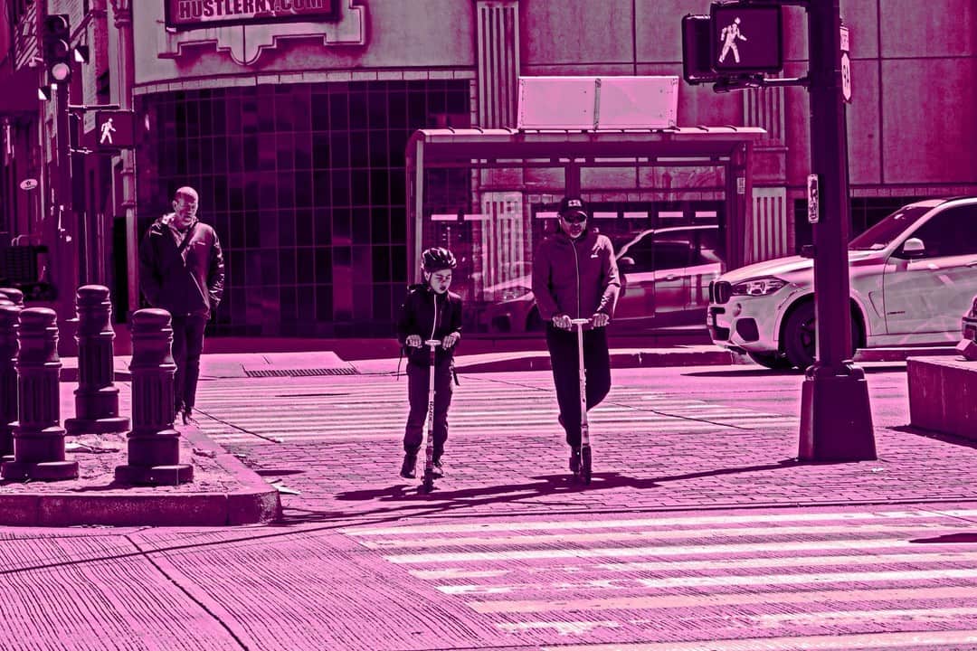 Cruce de calles con dos personas en patinete, con toda la imagen virada a rosa.