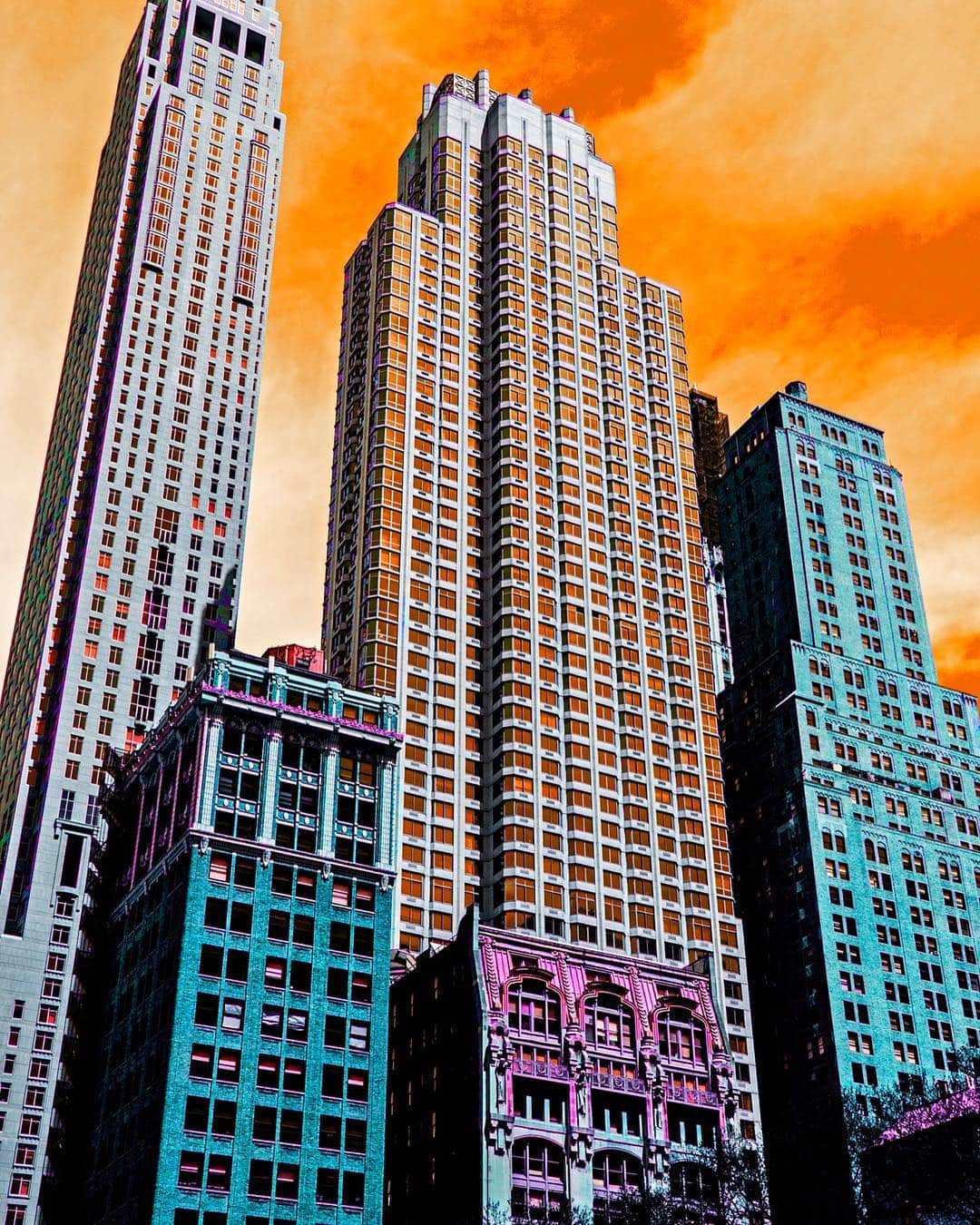 Rascacielos de Nueva York con las fachadas viradas a turquesa, rosa y naranja, bajo un cielo anaranjado.