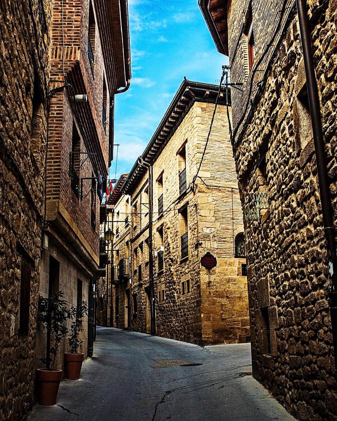 Calle empedrada de Laguardia entre casas de piedra con balcones, bajo un cielo azul.