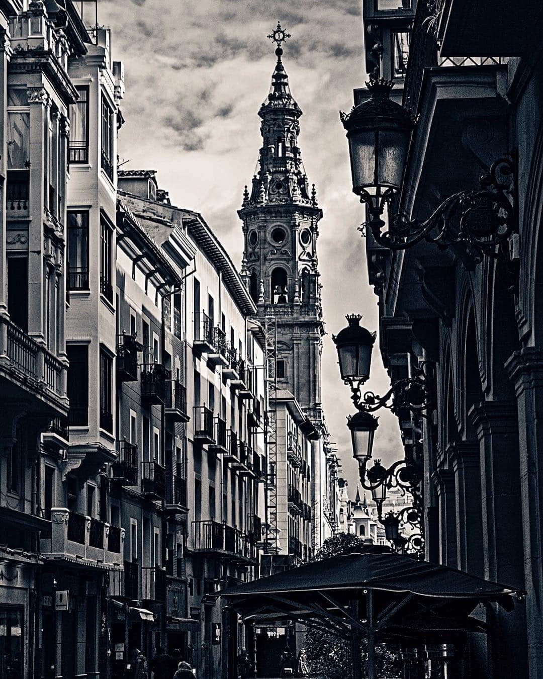 Calle de Logroño en blanco y negro, con edificios de balcones y una torre barroca al fondo.