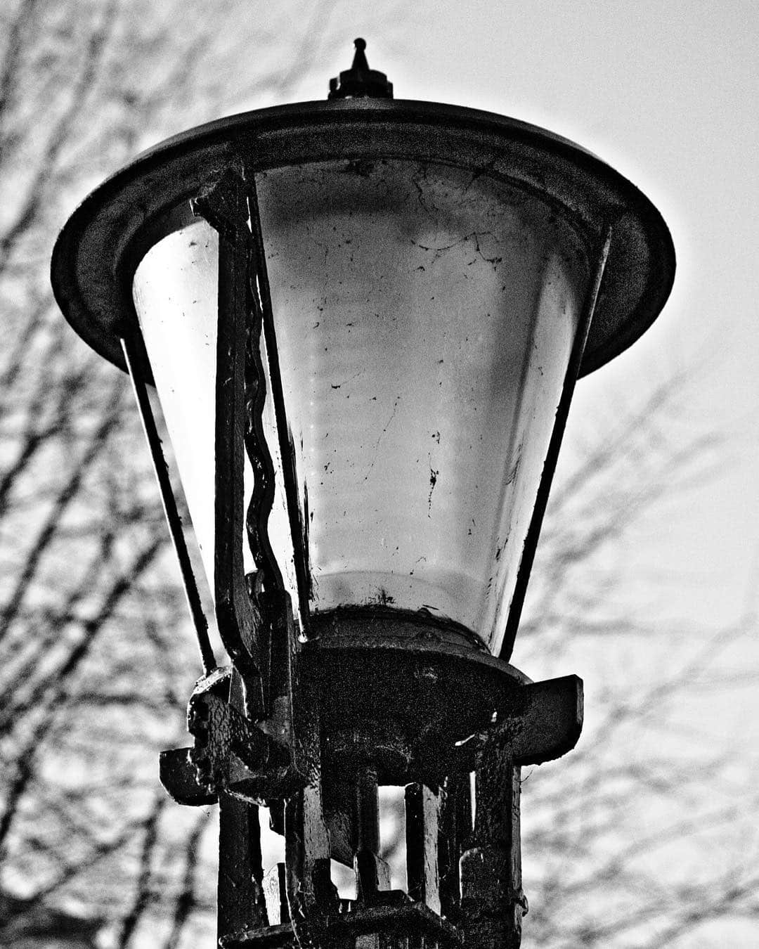 Farol de calle antiguo visto de cerca en blanco y negro, con el cristal y la estructura de hierro muy contrastados.