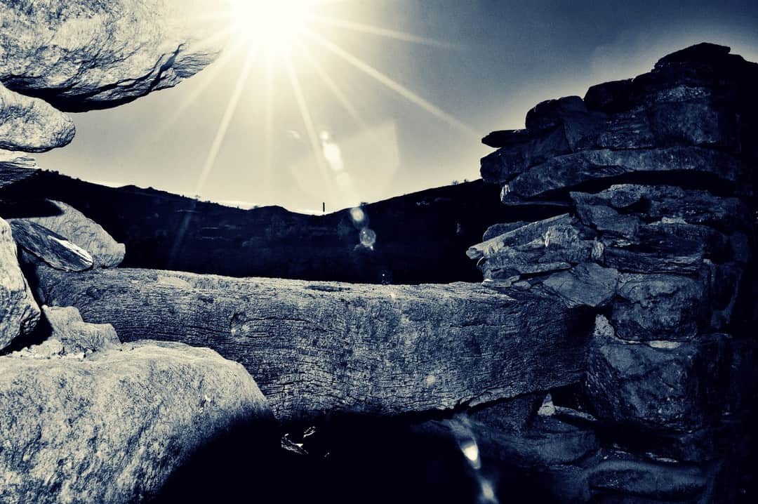 Rocas y un arco de piedra a contraluz, con el sol en estrella asomando por el borde.