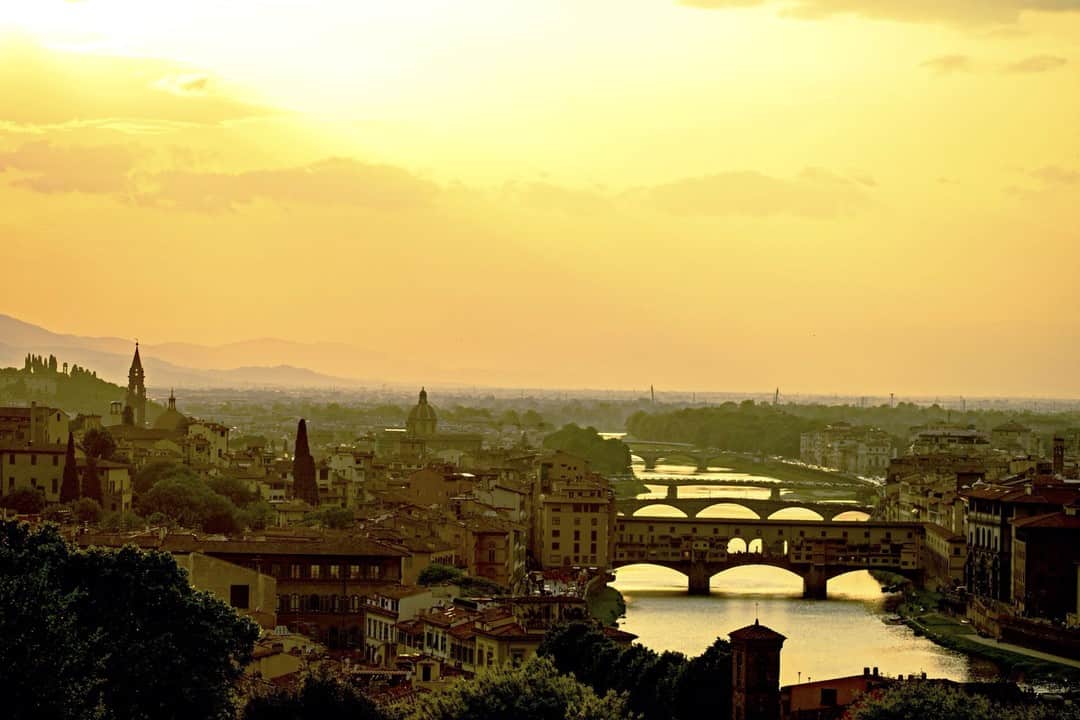 Florencia al atardecer desde lo alto, con los puentes sobre el Arno y el cielo dorado.
