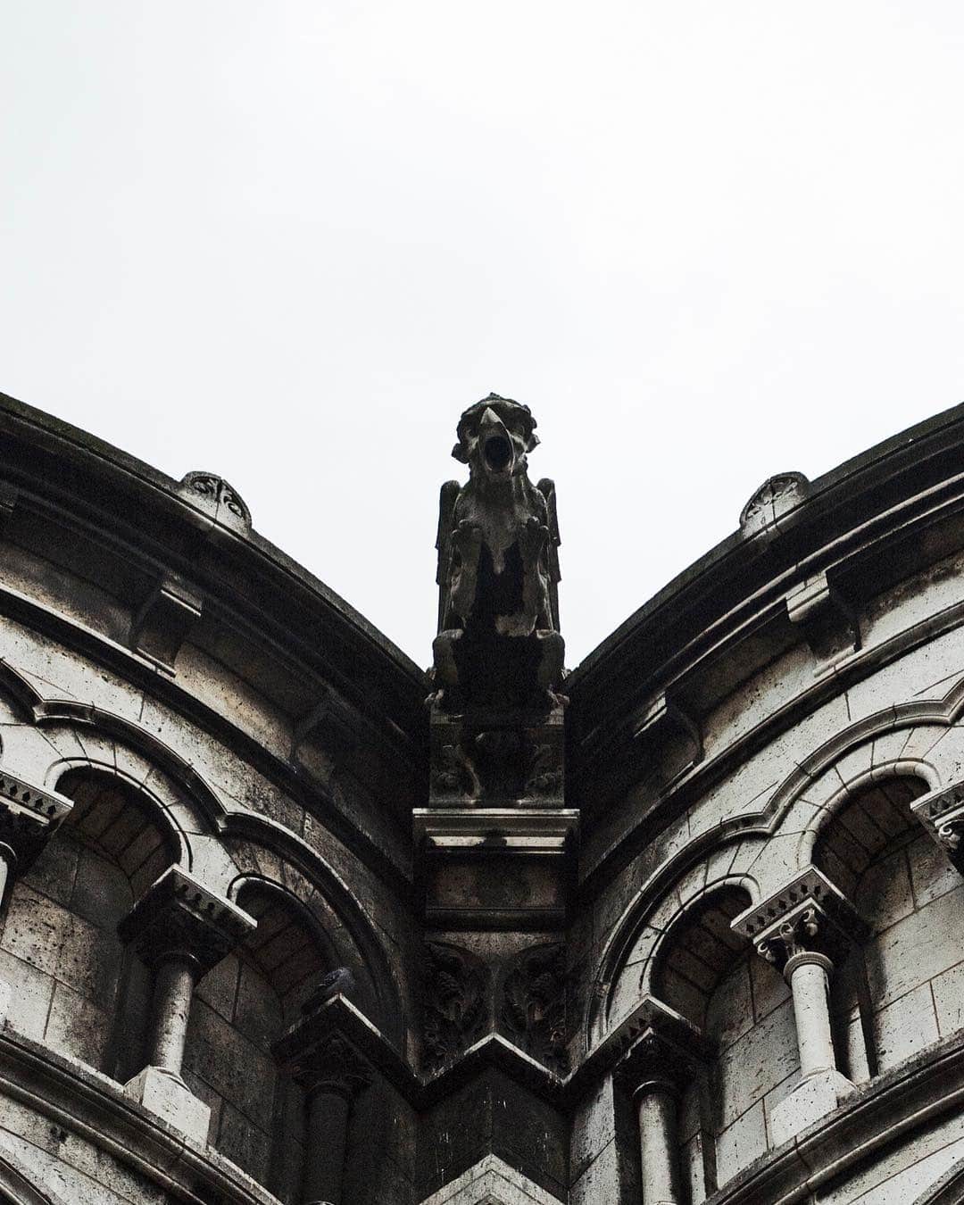 Ábside de piedra de una iglesia visto desde abajo, con una gárgola en lo alto, en blanco y negro.