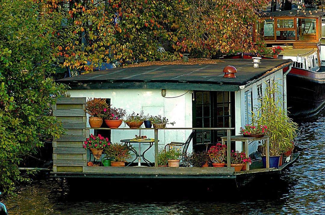 Casa flotante con la terraza llena de macetas y plantas, amarrada en un canal en otoño.