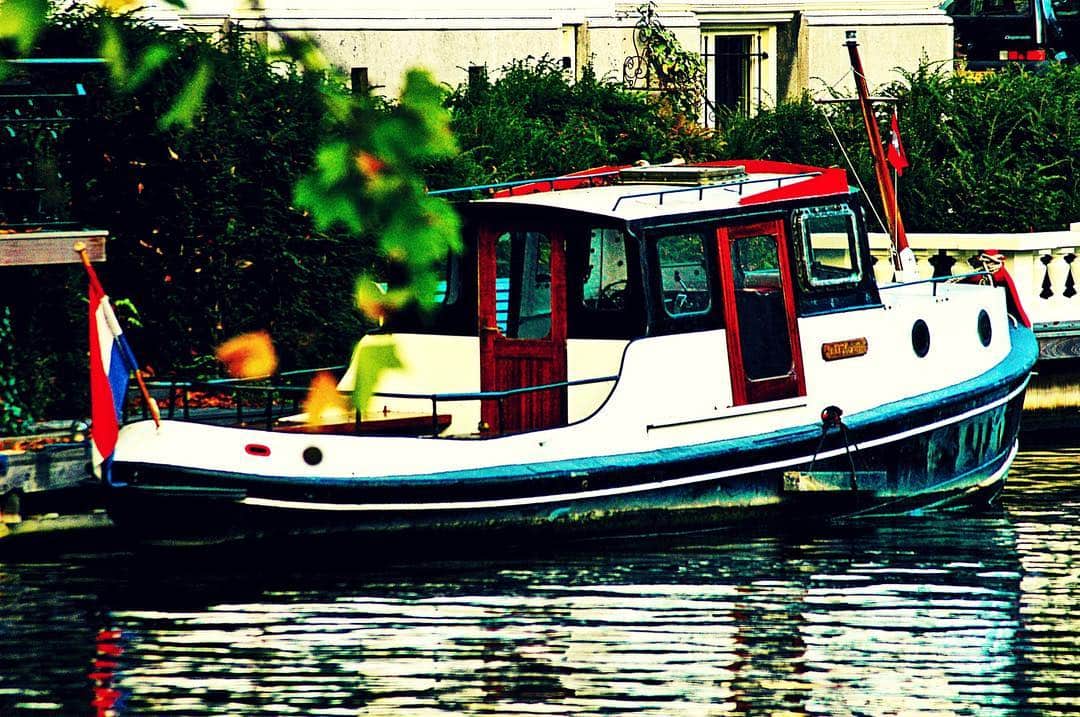 Barca de recreo blanca y roja amarrada en un canal, con vegetación en las dos orillas.