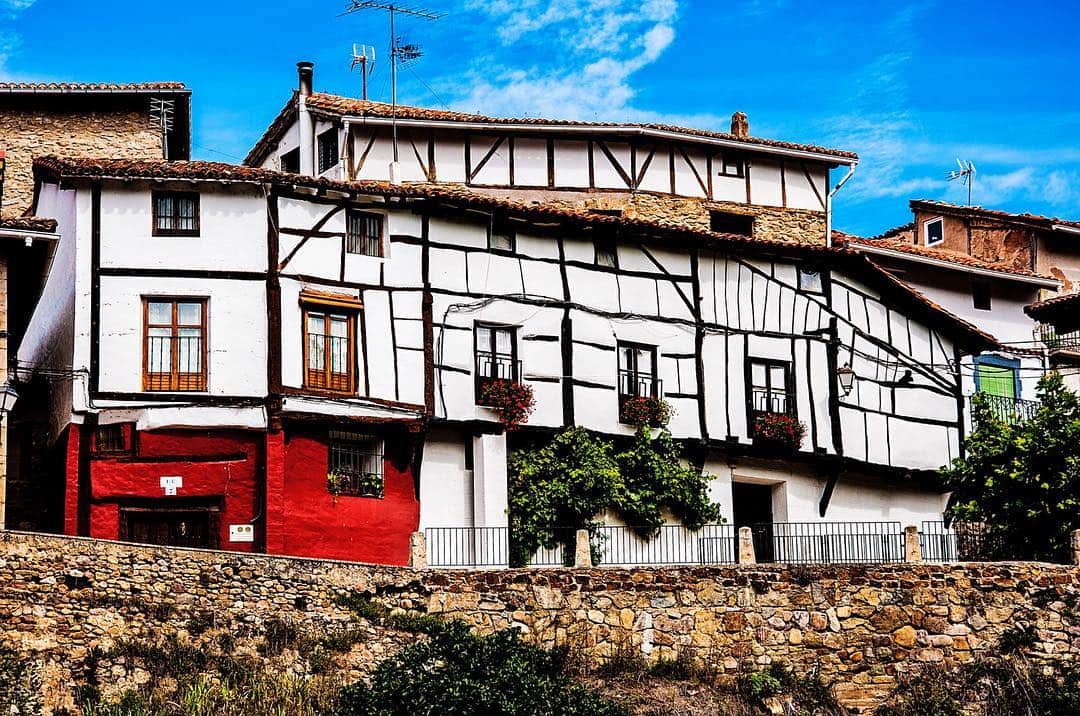 Casa de pueblo con entramado de madera blanco y negro, balcones de flores y un zócalo de piedra.