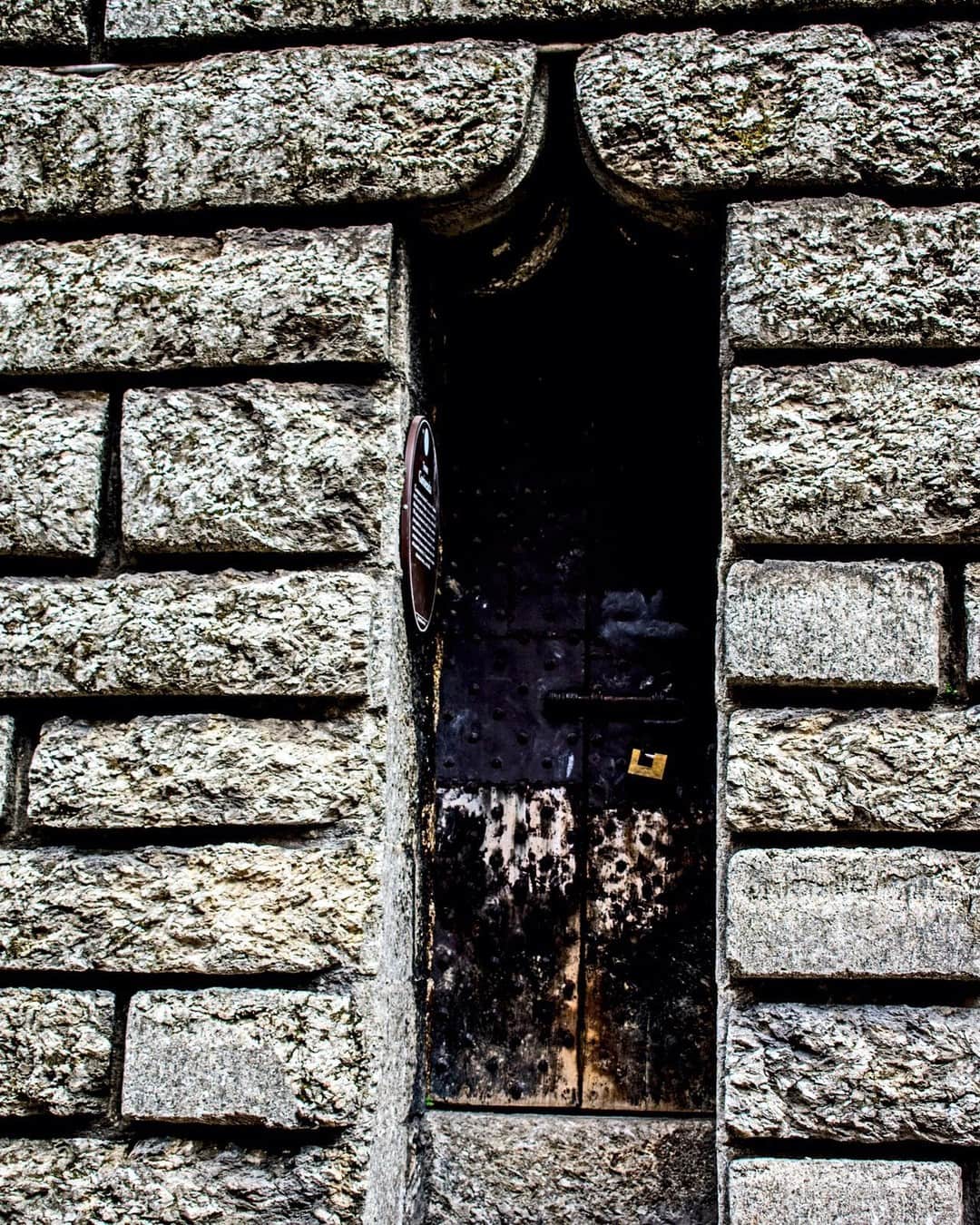 Puerta estrecha y oscura en un muro de sillares de piedra muy erosionados.