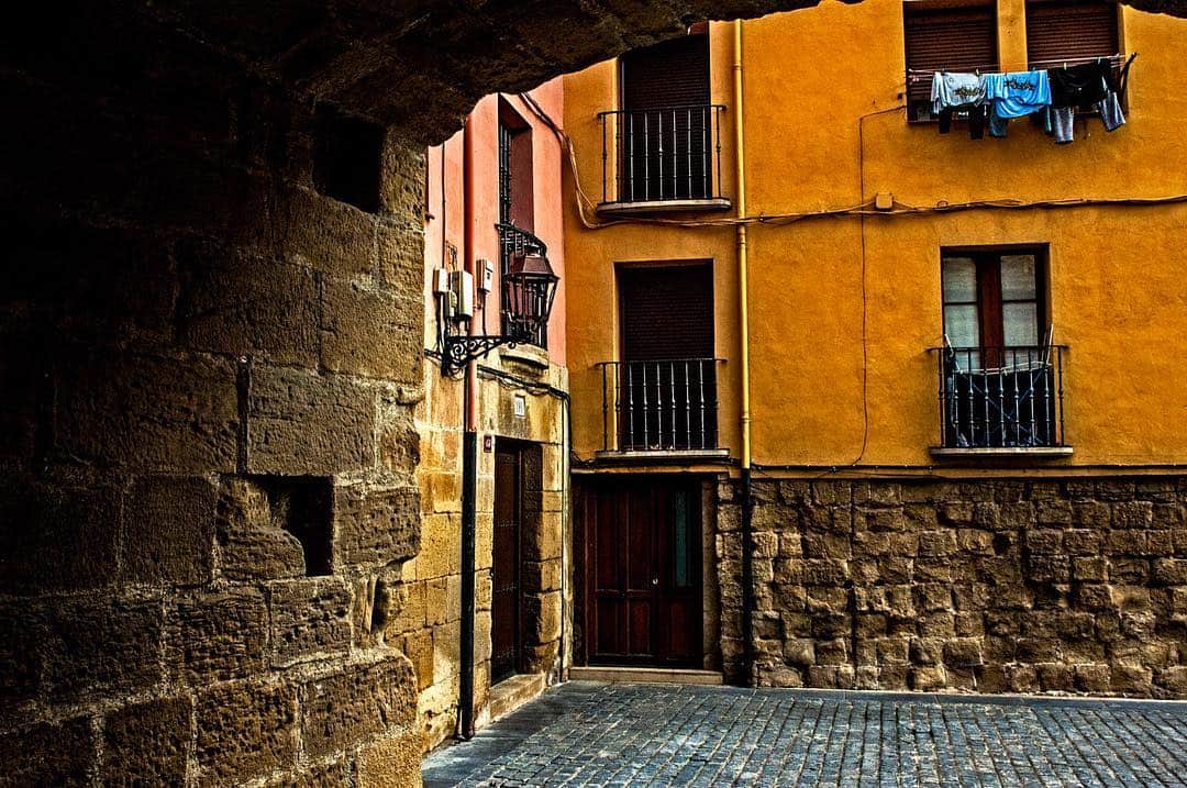 Rincón de un casco antiguo con una casa de fachada amarilla y balcones, vista desde un pasadizo de piedra.