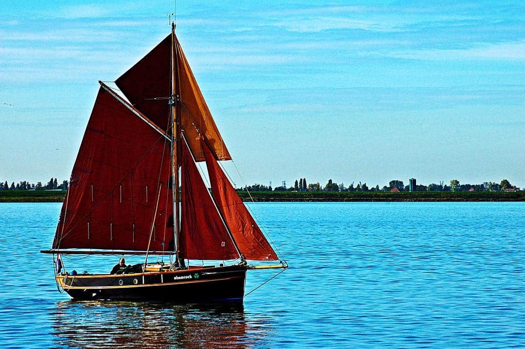 Velero de vela roja navegando en aguas turquesas bajo un cielo despejado.