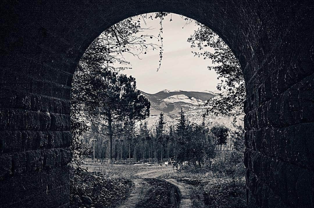 Vista de un valle a través de un arco de piedra, enmarcada por el muro oscuro, en blanco y negro.