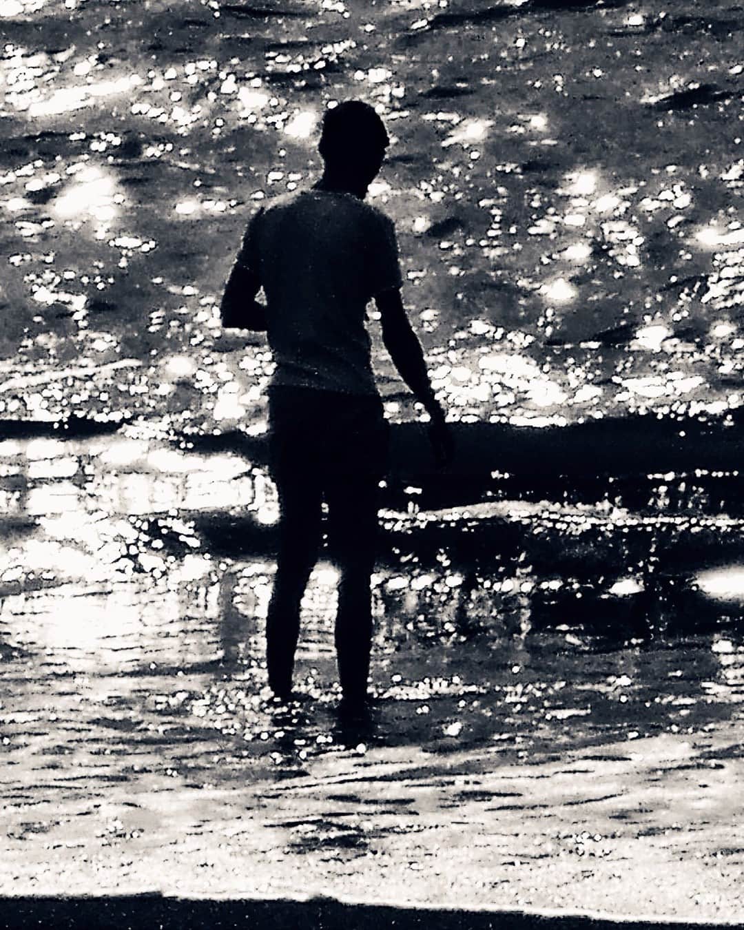 Silueta de una persona de pie en la orilla, recortada contra el agua llena de reflejos, en blanco y negro.