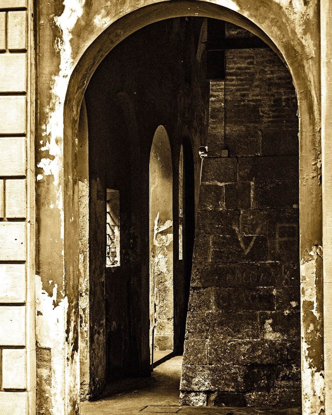Arcos de piedra superpuestos en la base de una torre medieval, en tonos sepia.