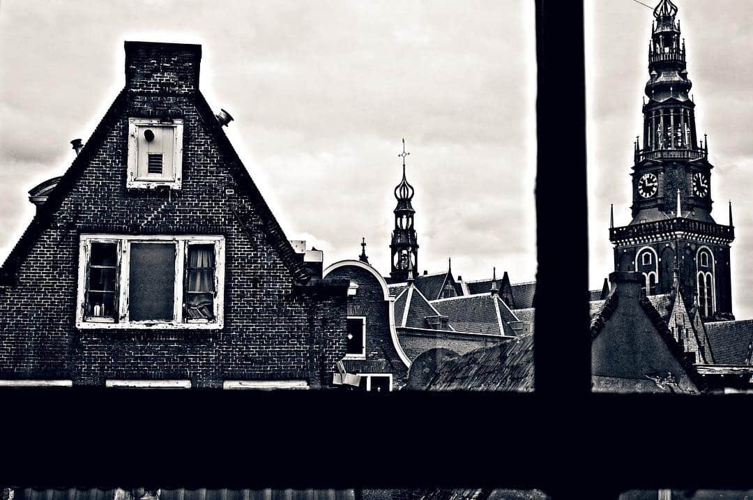 Tejados y torres de Ámsterdam vistos por una ventana, recortados en blanco y negro.