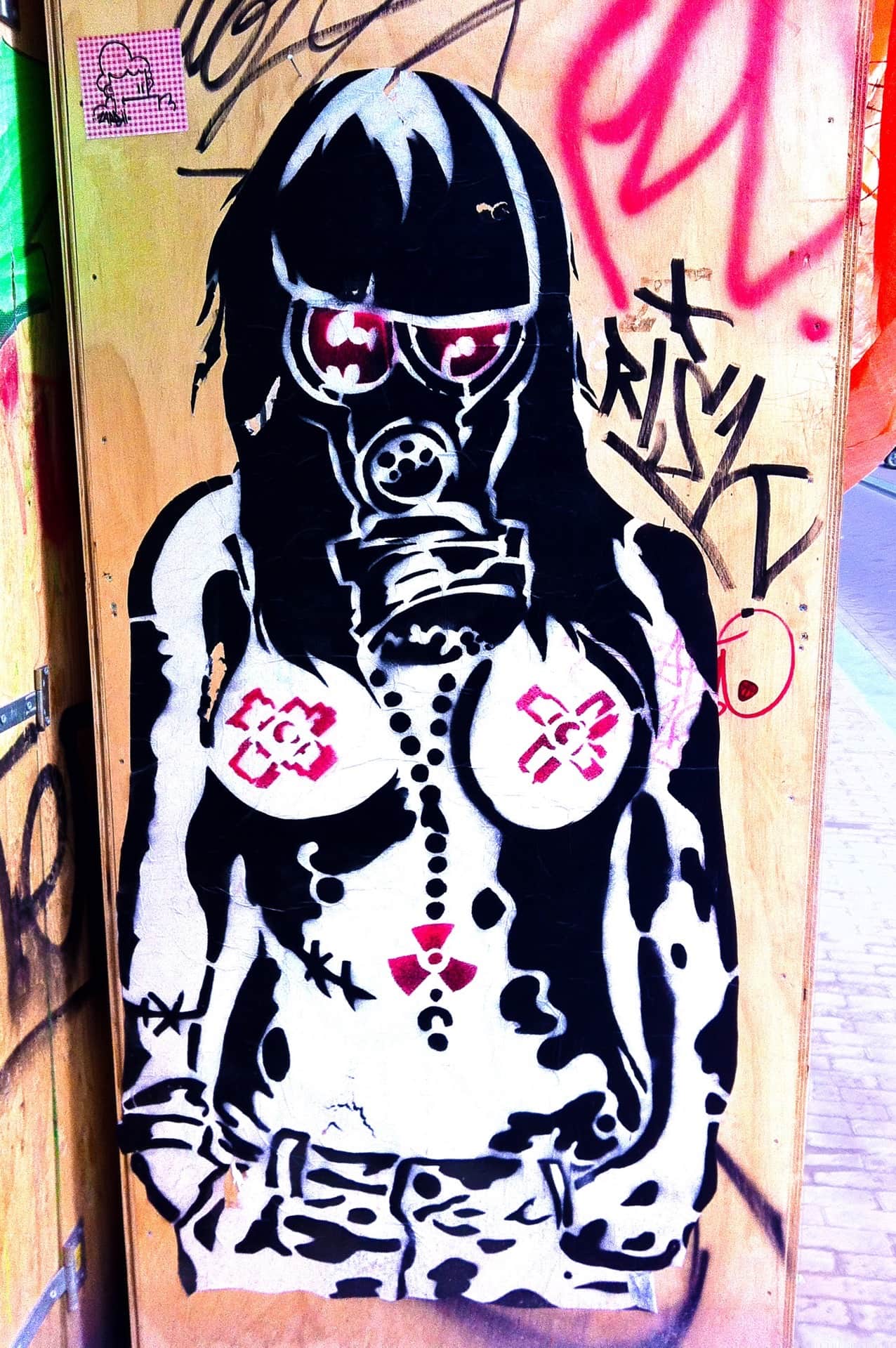 Grafiti de plantilla sobre un panel de madera: mujer de torso desnudo con máscara antigás y collar con símbolo radiactivo.