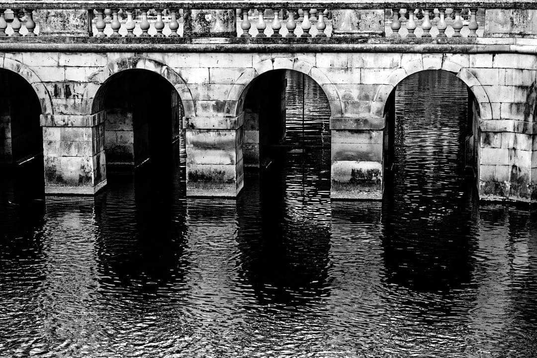 Arcada de piedra reflejada en el agua de un estanque, en blanco y negro.