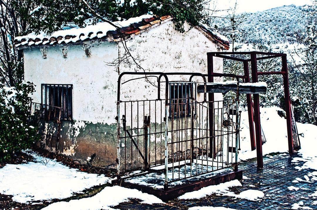 Caseta blanca de báscula con la puerta enrejada, bajo la nieve y junto a un armazón metálico oxidado.