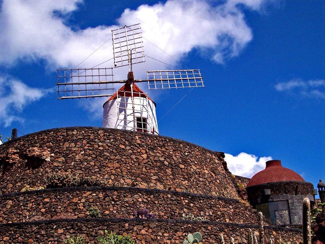 Molino de viento blanco sobre un tejado de teja curva, recortado contra un cielo azul con nubes blancas.