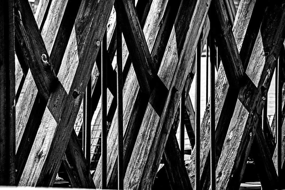 Estructura de vigas metálicas cruzadas de un puente, vista en diagonal, en blanco y negro.